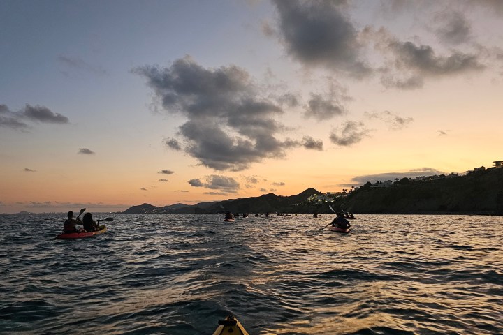 People kayaking on the sea at sunset with clouds and distant hills.