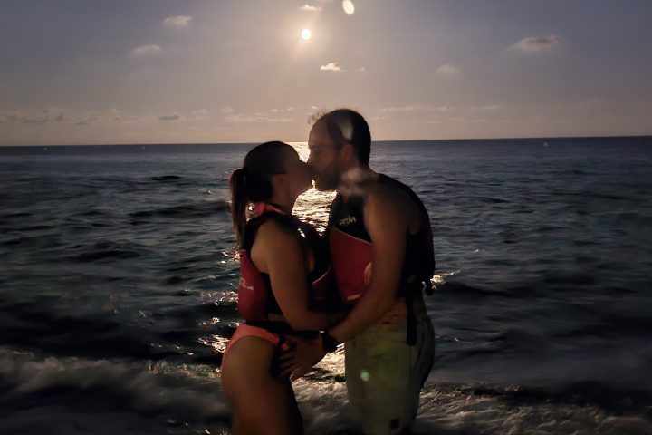 Couple kissing on a beach at sunset with ocean in background.