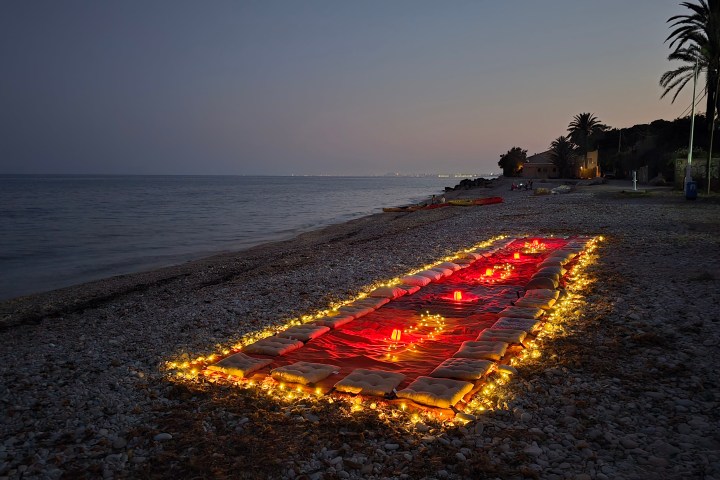 Beach at dusk with a long red carpet lined with fairy lights and pillows.
