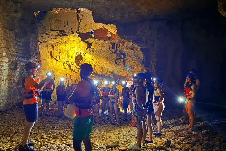 Group of people with helmets and lights exploring an illuminated cave.