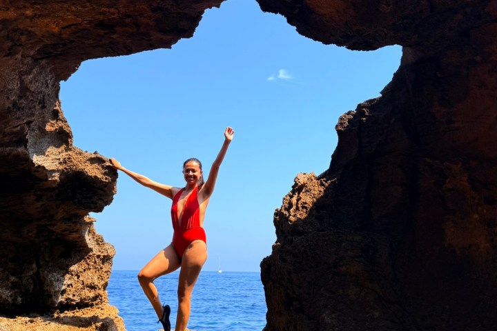 Person in red swimsuit posing on rocky arch by the sea.