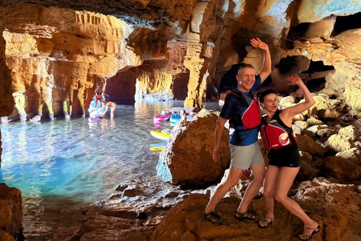 People in life vests waving inside a cave with kayakers in the background.