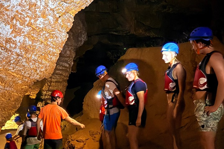 People in helmets exploring a cave with rocky walls.