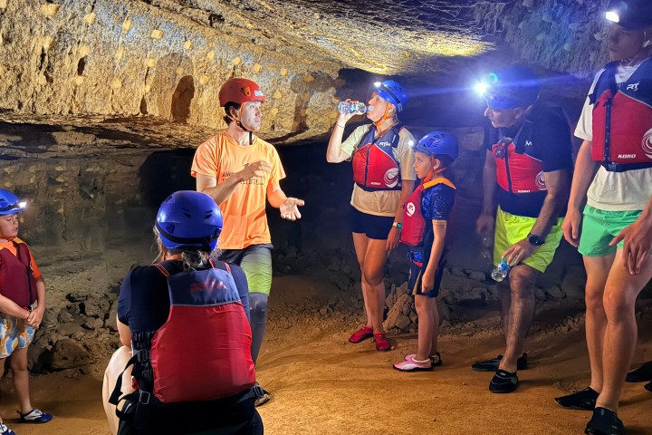 Group wearing helmets and vests exploring a cave with headlamps.