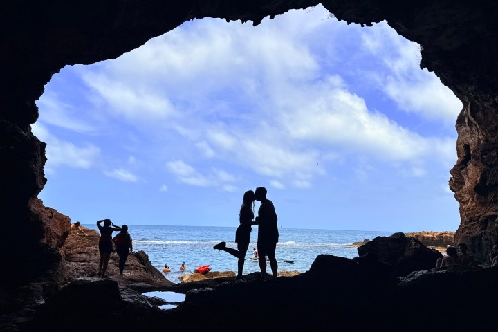 Silhouetted couple kissing in a sea cave with ocean view.