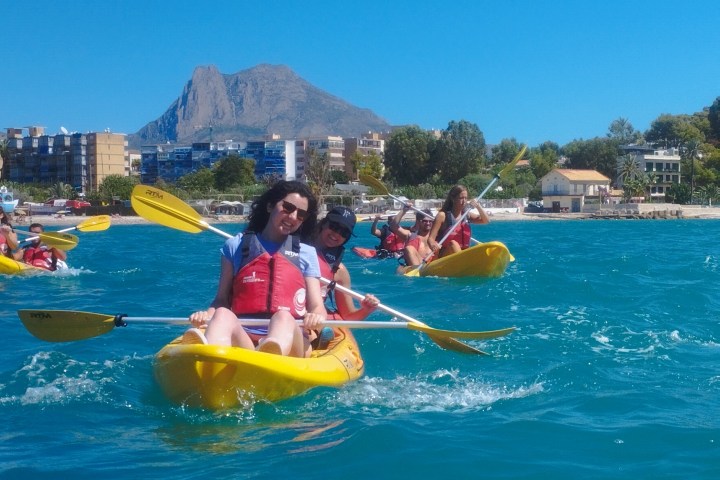 People kayaking in the ocean with a mountain and buildings in the background.
