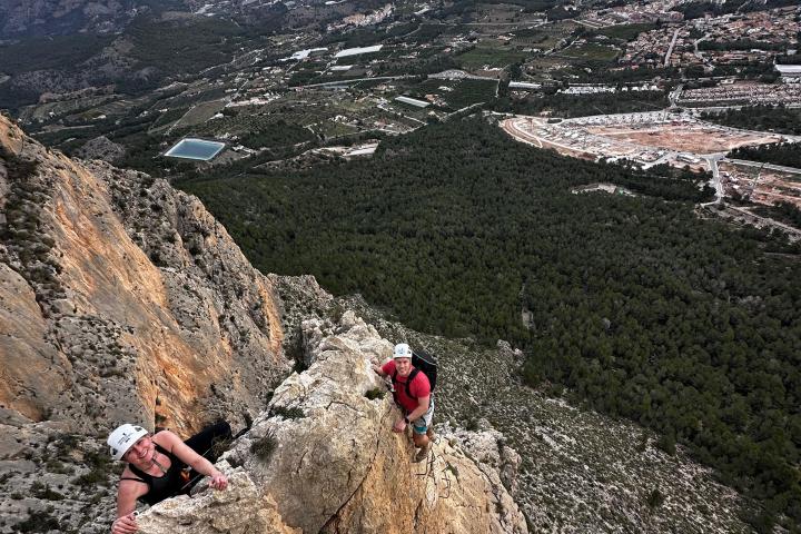 Two climbers ascending a rocky cliff with a vast landscape in the background.