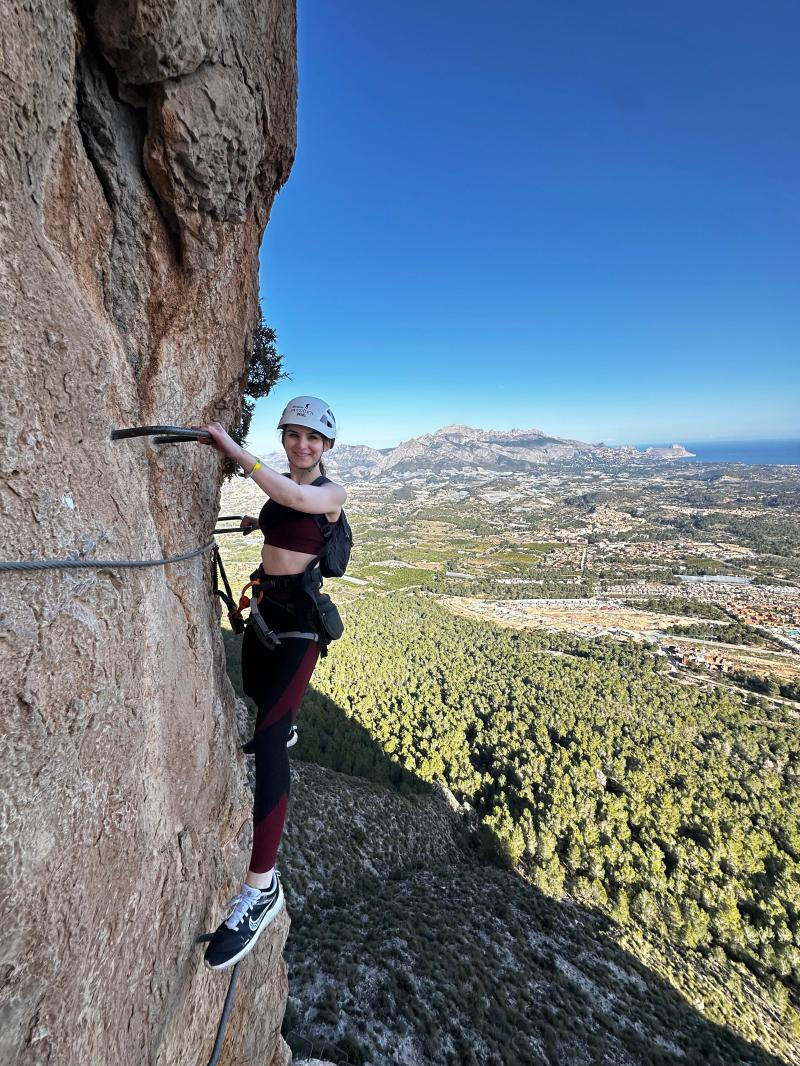 Person climbing a steep rock face with a distant view of mountains and landscape.