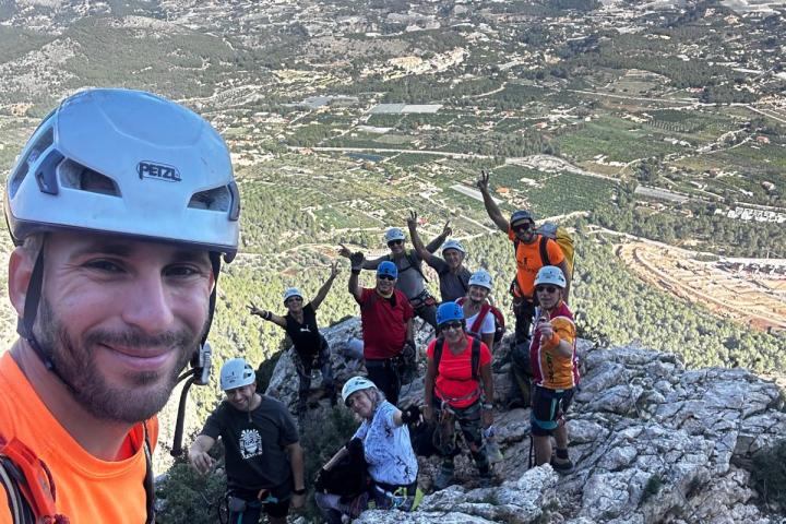 Group of climbers with helmets posing on a rocky mountain peak with a scenic valley view.