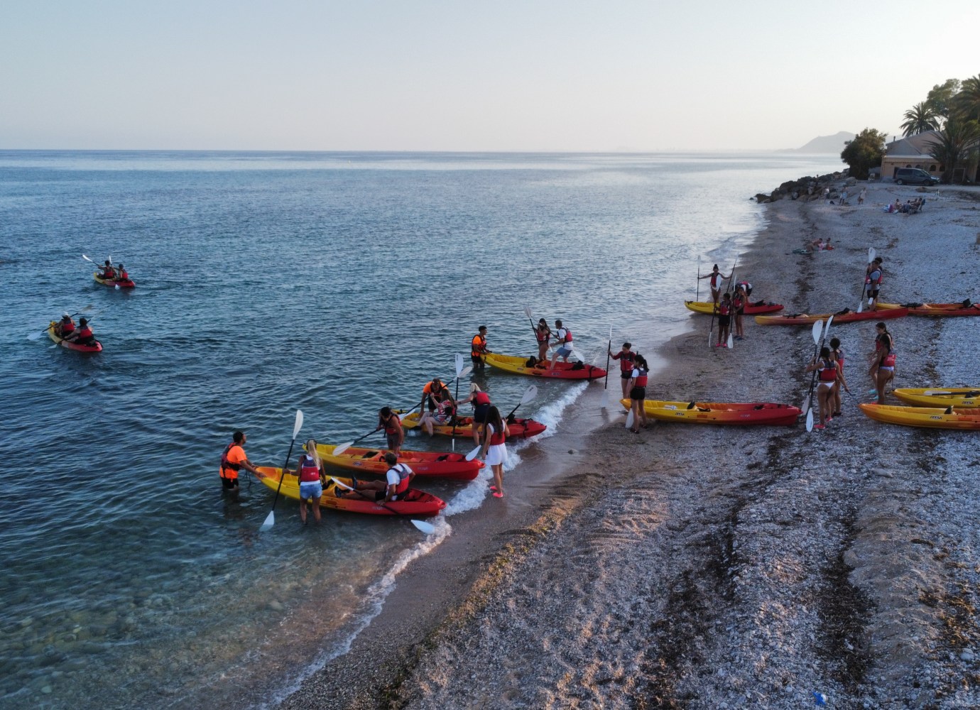 People in life jackets kayaking near a pebbled beach at sunset.