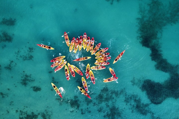 Aerial view of a group of colorful kayaks forming a circle on turquoise water.