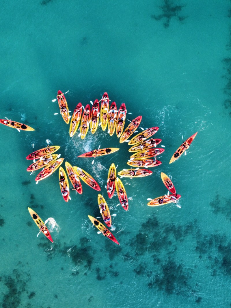 Aerial view of a group of colorful kayaks forming a circle on turquoise water.