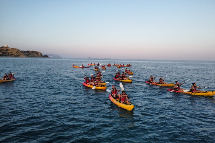 Group of people kayaking on calm ocean waters near rocky coastline at sunset.