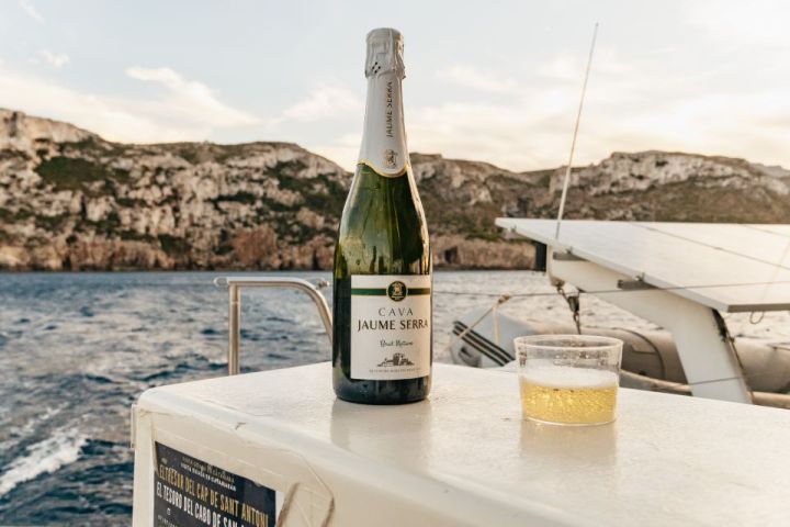 Bottle of cava and glass on a boat with rocky coastline in the background.