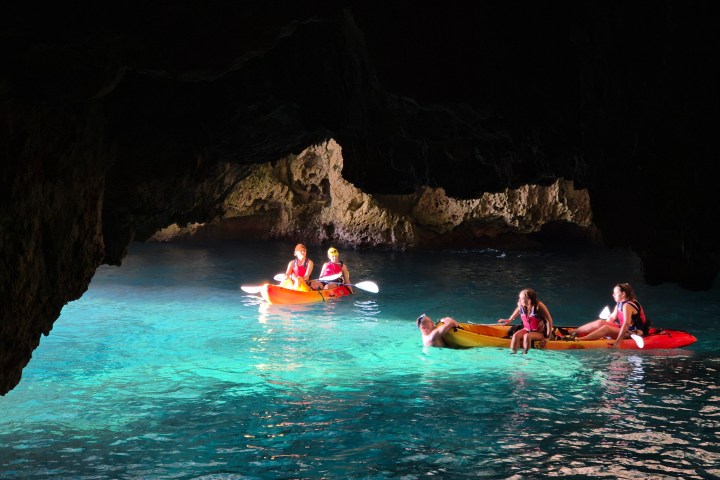 People kayaking in a cave with turquoise water and illuminated rocky walls.