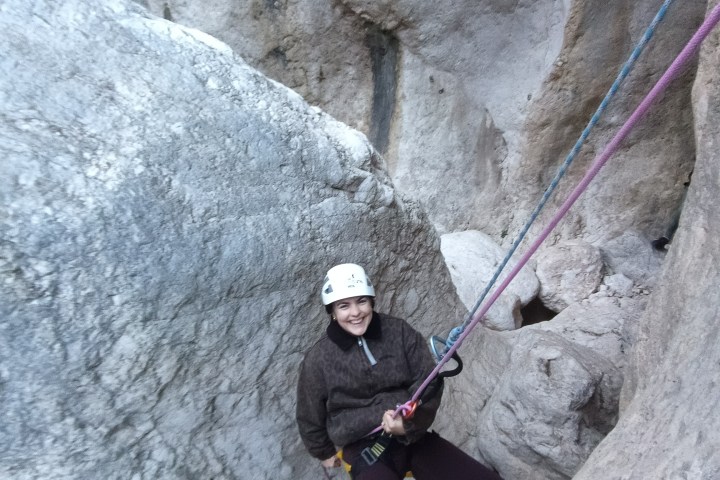 Person rock climbing with ropes, wearing a helmet, smiling in a canyon.