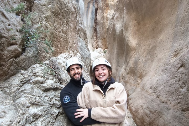 Couple smiling in canyon, wearing helmets and climbing gear, surrounded by large rock walls.