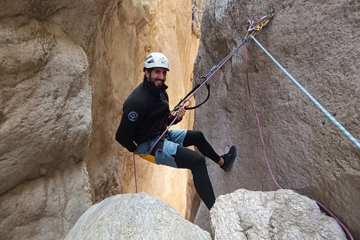 Person in climbing gear rappels between rocky canyon walls.