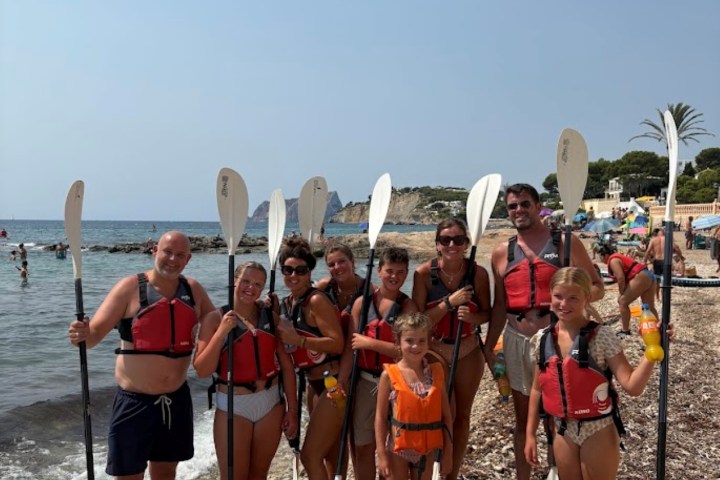 Group of people in red life vests holding paddles on a rocky beach.