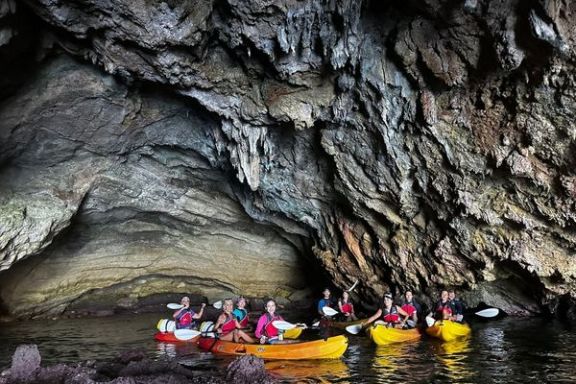 Grupo de kayaks explorando una gran cueva marina en la Cala Granadella
