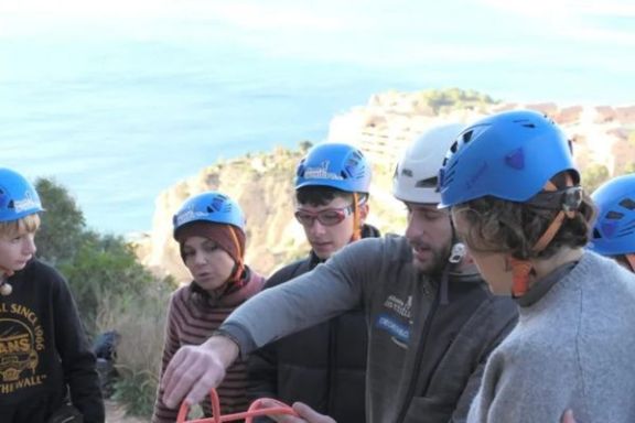 Técnico deportivo mostrando el manejo de las cuerdas a varios participantes durante un bautismo de escalada en Altea.