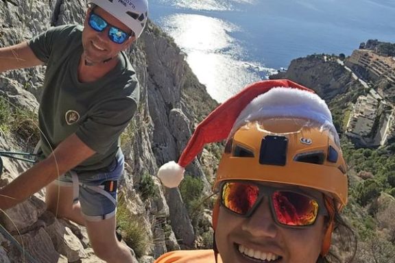 Dos escaladores sonrientes con casco y arnés en las paredes del Morro de Toix, con el mar Mediterráneo de fondo.