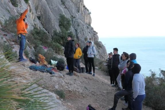 Técnico deportivo explicando las técnicas básicas de escalada a un grupo de participantes junto al Mediterráneo.