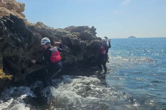 Participantes avanzando entre las rocas y el agua durante una actividad de coasteering