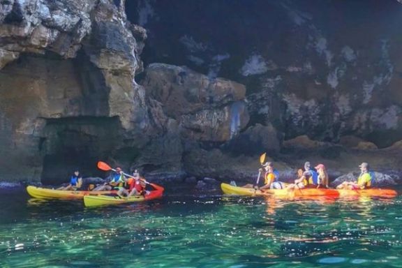 Grupo navegando en kayak frente a la entrada de la Cova Tallada durante una ruta guiada