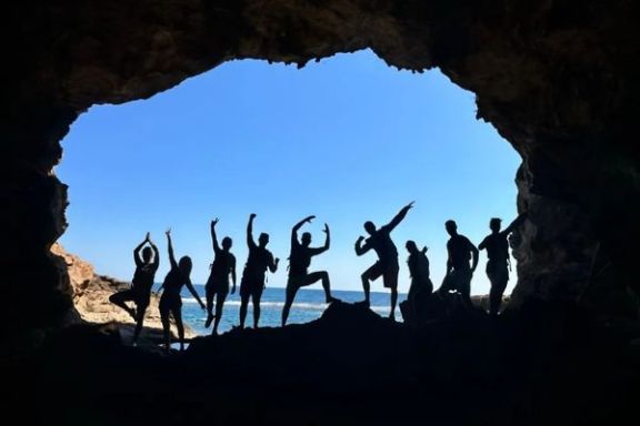 Silueta de un grupo de participantes en la entrada de la Cova Tallada con el mar al fondo