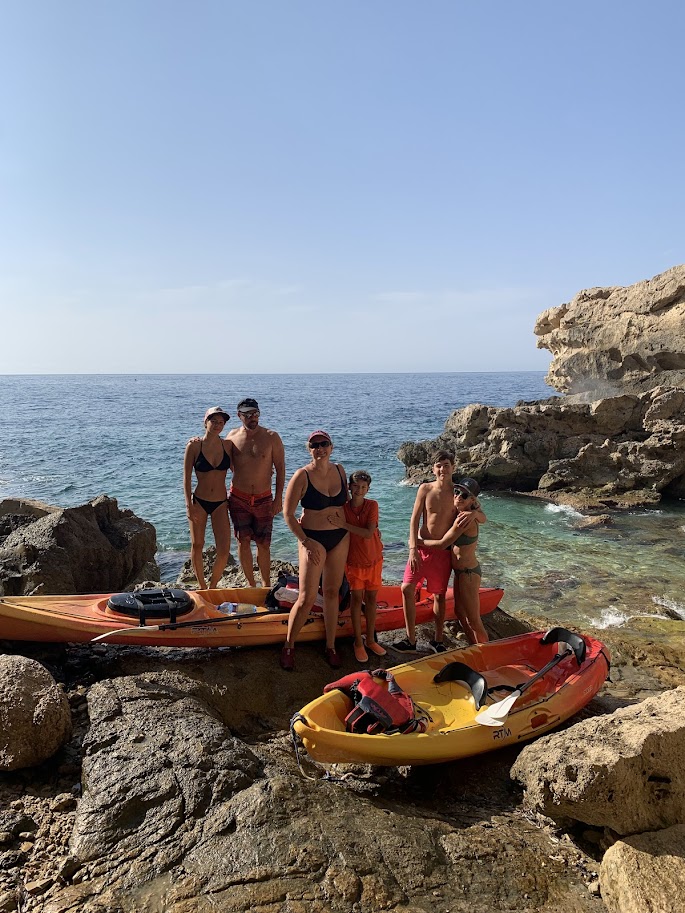 Group of people in swimwear with kayaks on rocky shore by the sea.