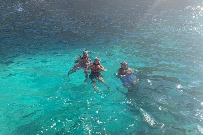 Three snorkelers floating in clear blue water by a rocky shore.