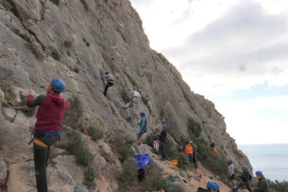 Participantes escalando y asegurando con cuerdas en una pared de roca durante una actividad en Elda.