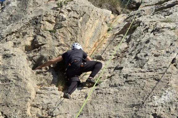 Escalador ascendiendo por una pared de roca con cuerda de seguridad en Elda, Alicante.