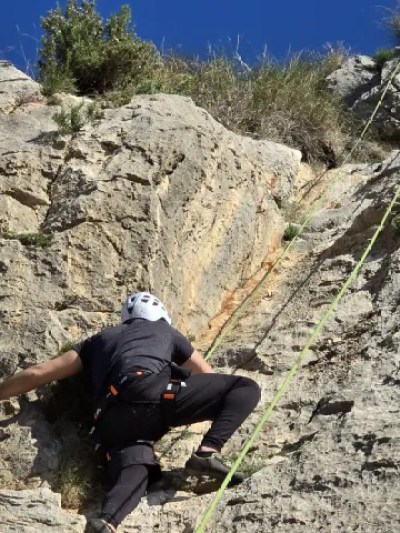 Rock climber ascending a cliff with a rope under a clear blue sky.