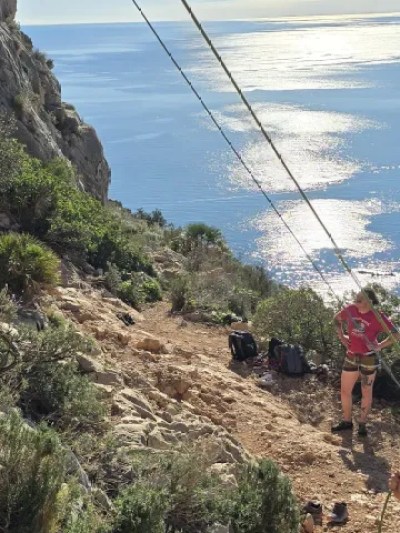Group rock climbing on a coastal cliff with ocean in the background.