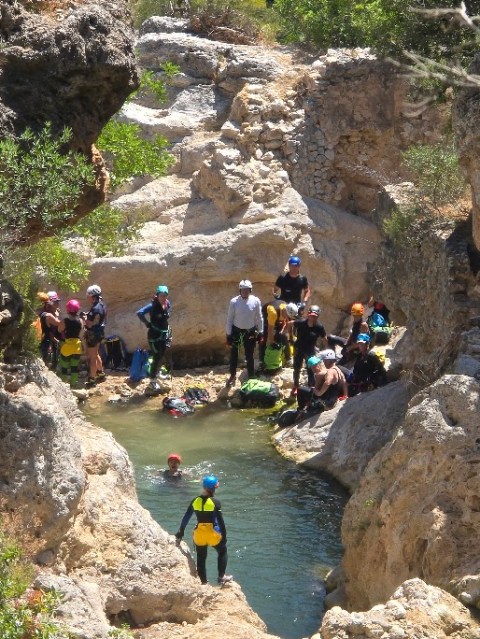 Group of people with helmets gathered near a rocky stream in a canyon area.