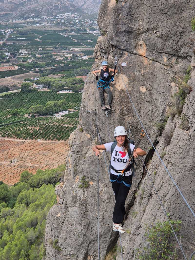 Two people climbing a rocky mountain via ferrata with a scenic valley view.