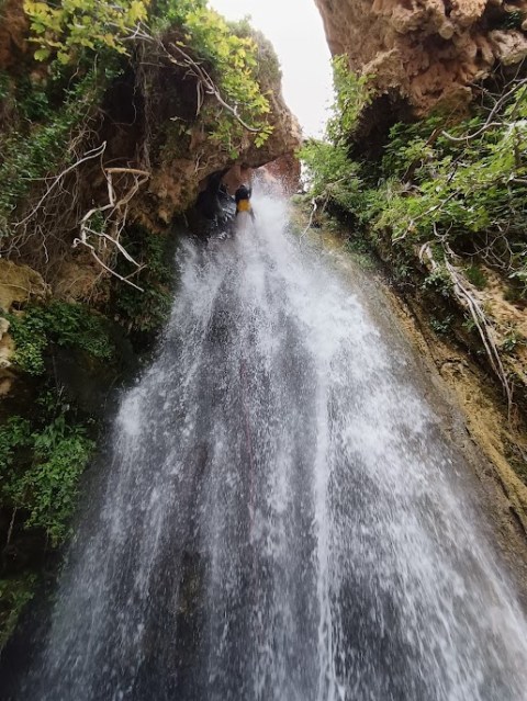 Person rappelling down a waterfall surrounded by rocky cliffs and greenery.
