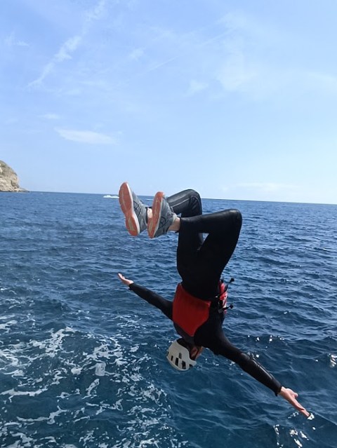 Person in mid-air backflip over ocean, wearing helmet and red life jacket.