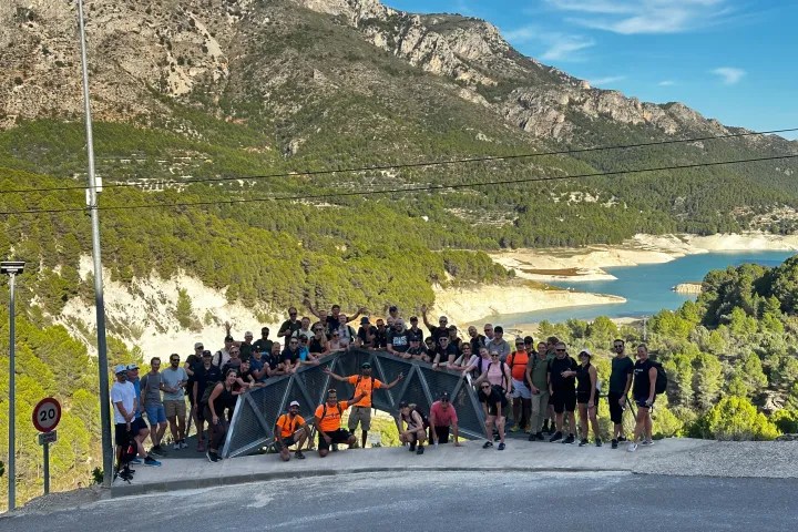 Large group of people on a walkway with mountainous landscape and lake in the background.