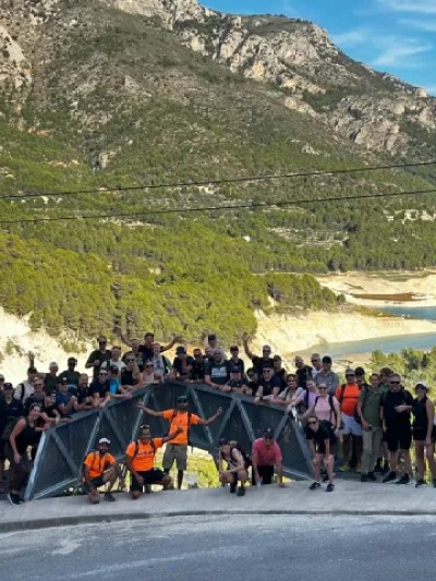 Large group of people on a walkway with mountainous landscape and lake in the background.