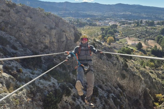 Person suspended on a high rope crossing a canyon with clear sky and mountains in the background.