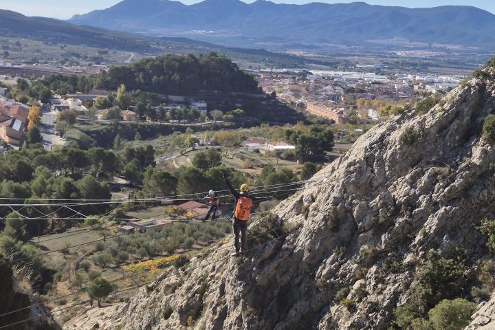 Person hiking on a steep rocky mountain with a scenic valley and mountains in the background.
