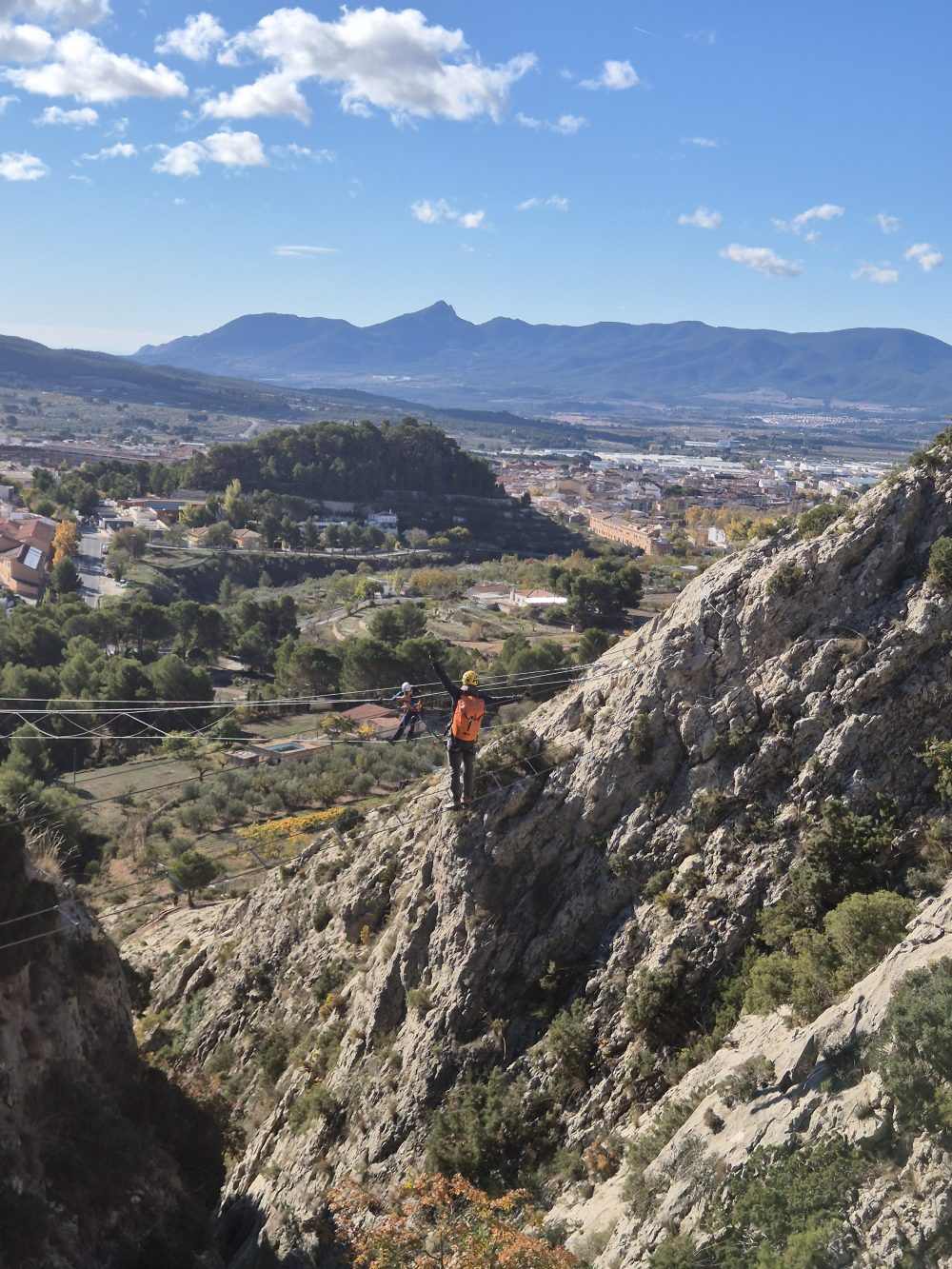 Person hiking on a steep rocky mountain with a scenic valley and mountains in the background.