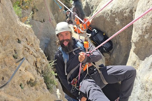 Two people canyoning with ropes in a narrow rocky gorge.