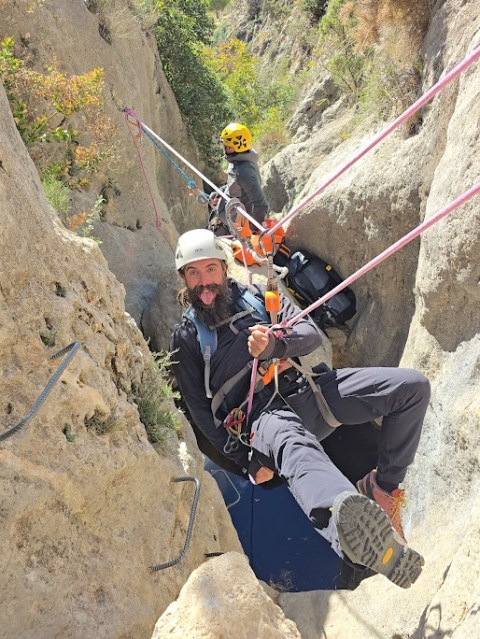 Two people canyoning with ropes in a narrow rocky gorge.