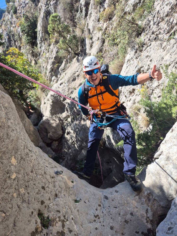 Climber in gear giving thumbs up while rappelling on a rocky cliff.