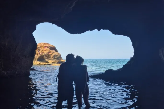 Silhouette of a couple standing in a cave by the sea.