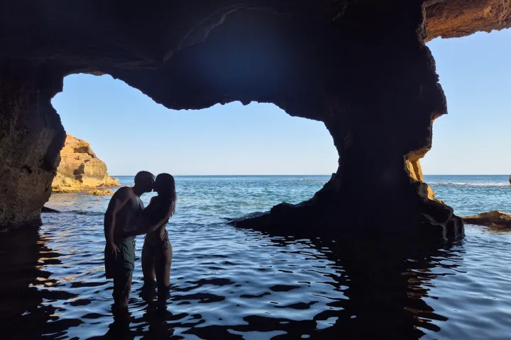 Silhouetted couple kissing inside a seaside cave with ocean view.
